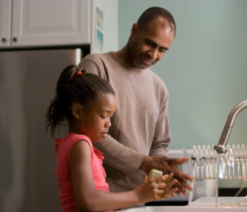 Parent and child washing their hands at kitchen sink.