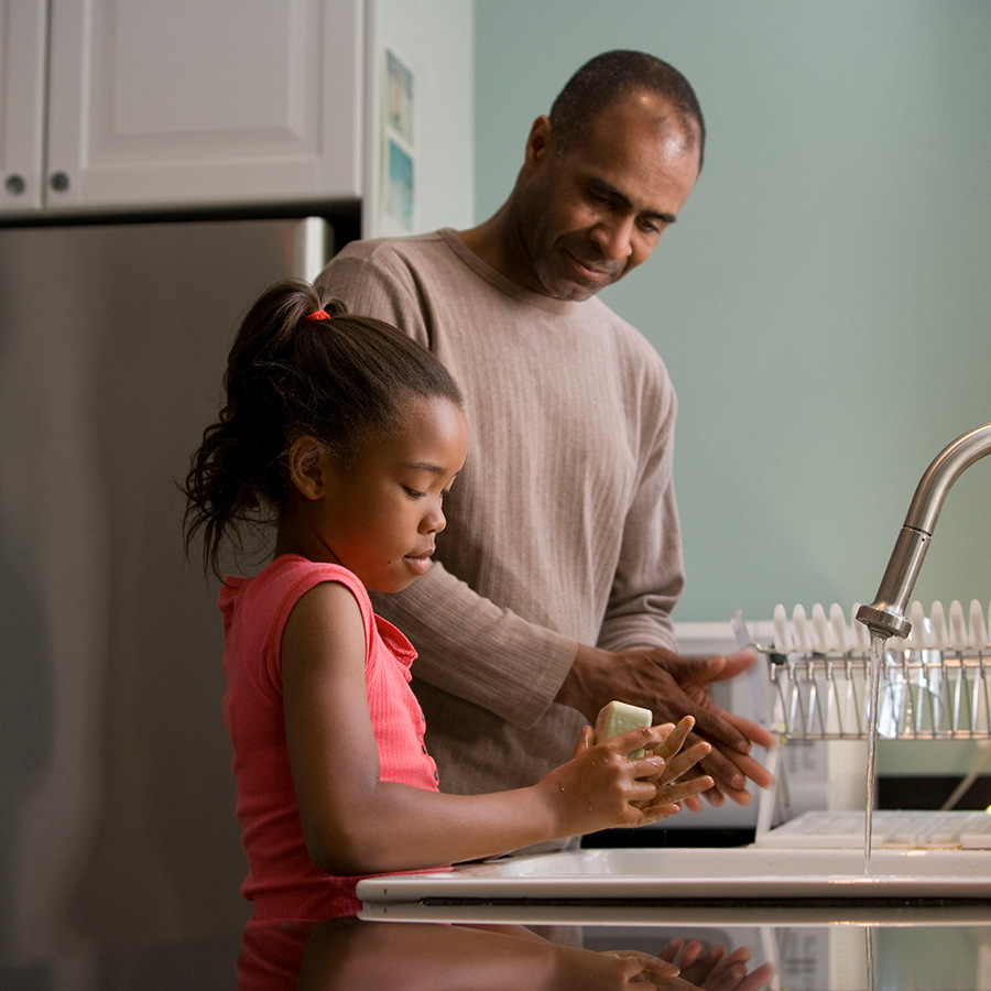 Parent and child washing their hands at kitchen sink.